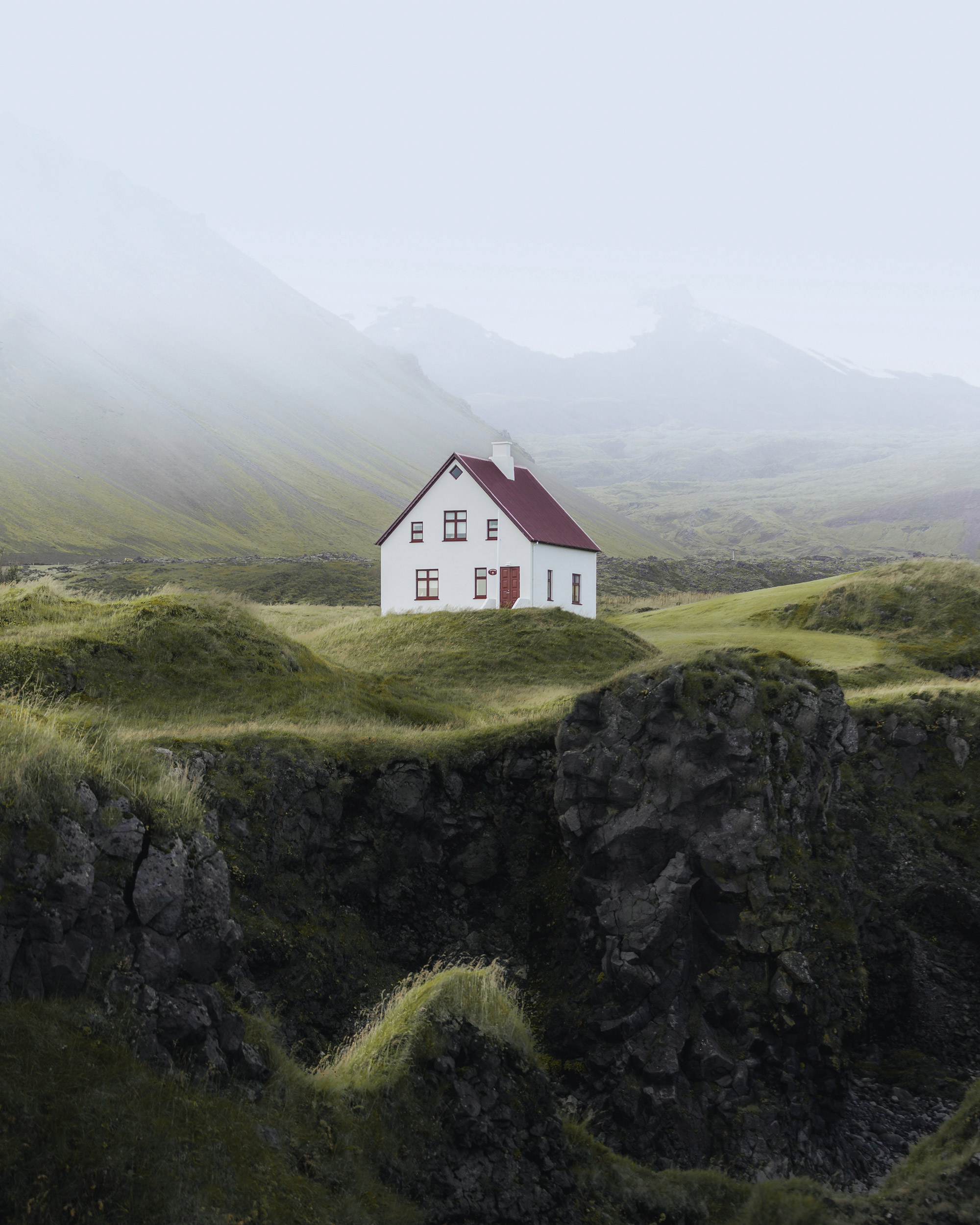The image features a white house situated on a hill, surrounded by a picturesque landscape. The scene includes grassy fields and mountains in the background
