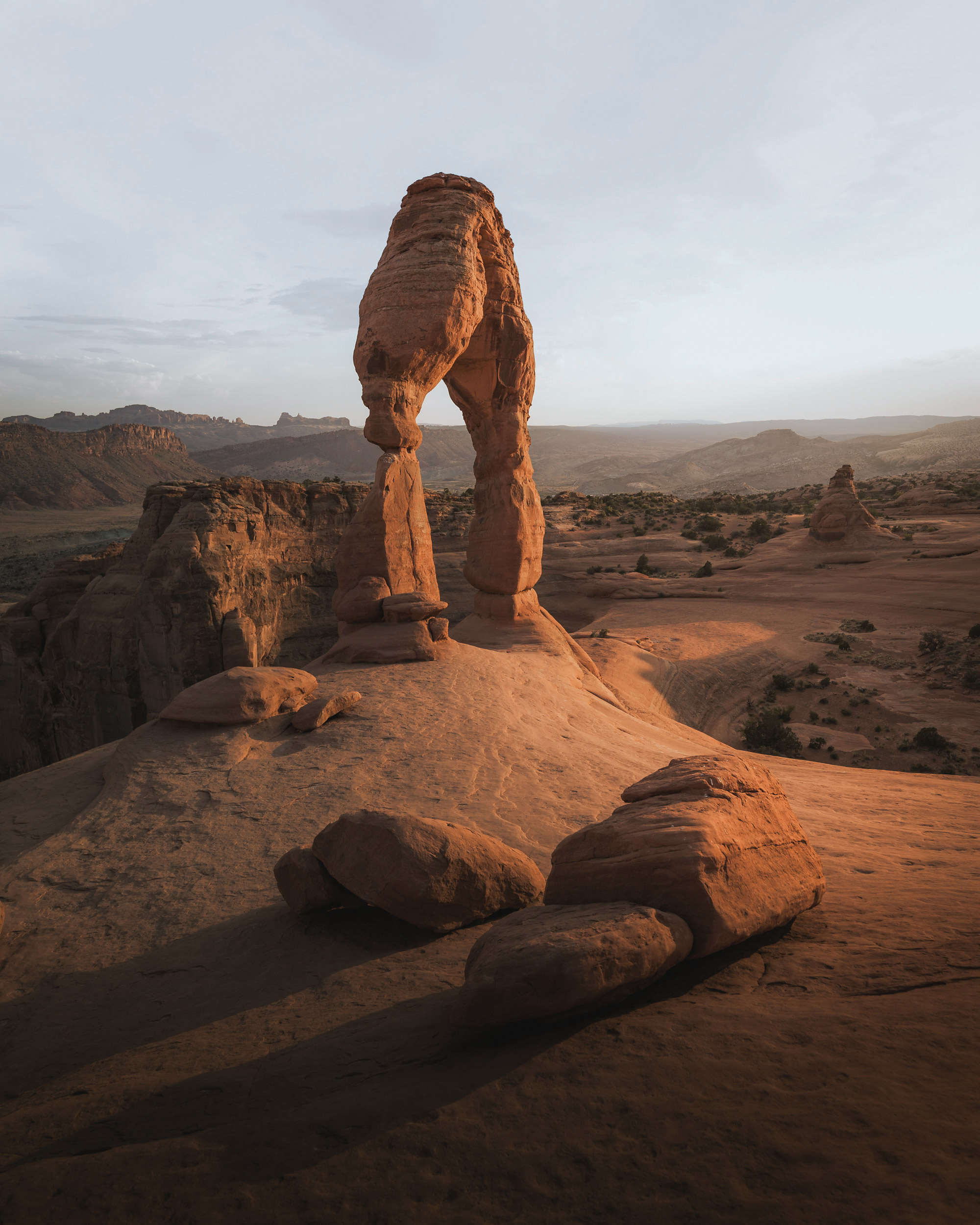 The landscape features elements like badlands, aeolian landforms, and formations of sand. The scene is enriched with a clear sky, highlighting the geological features around them, including a broken arch structure.