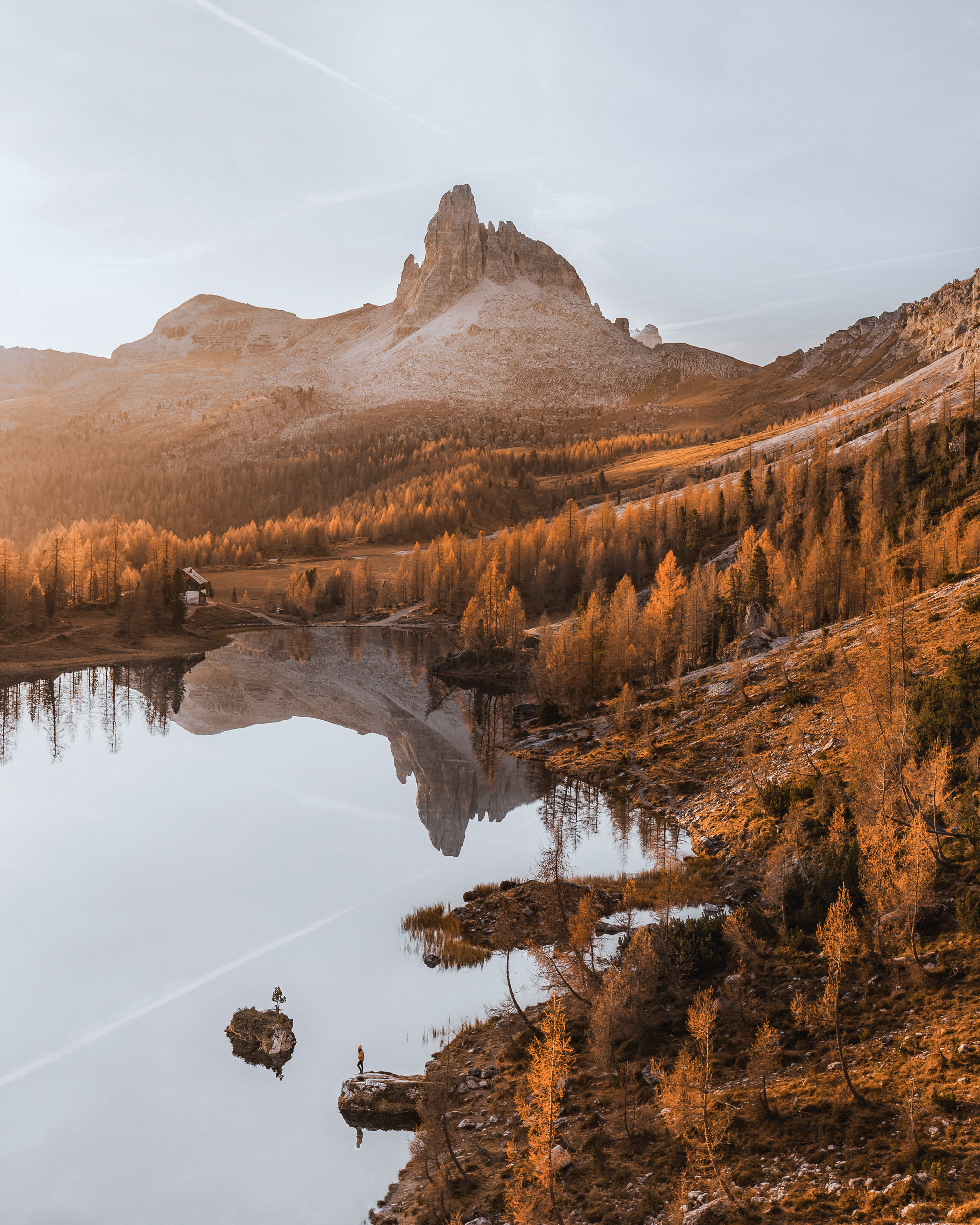 A calm lake reflecting golden larches and rugged peaks in the soft morning light.