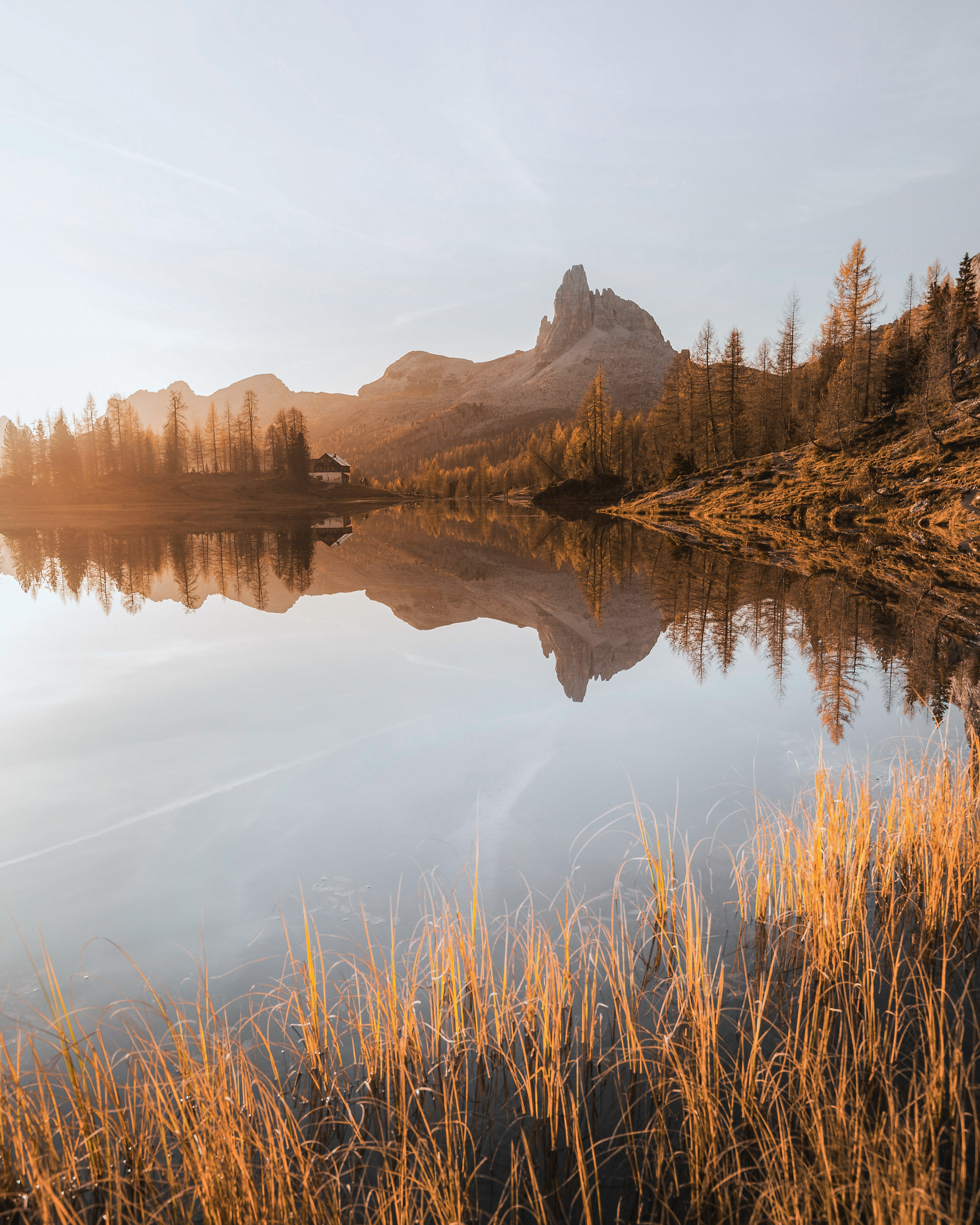 A serene landscape photograph captures a tranquil lake reflecting the surrounding mountains at sunrise or sunset.