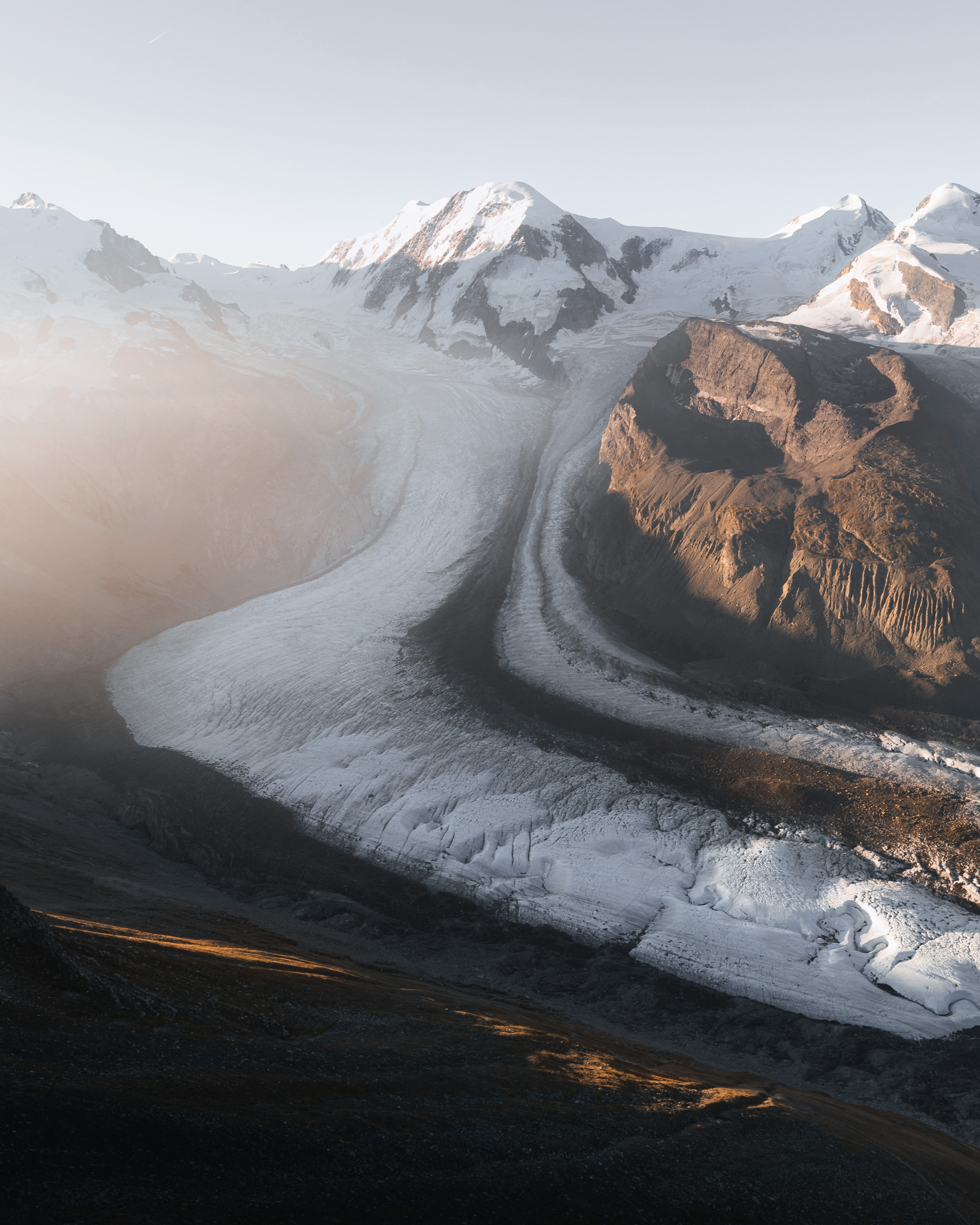 The image depicts a snowy mountain surrounded by a river, showcasing the beauty of nature in winter. The scenery includes elements such as a mountain range, glacial landform, and tundra terrain. The sky is likely filled with fog, adding to the serene atmosphere of this outdoor landscape.