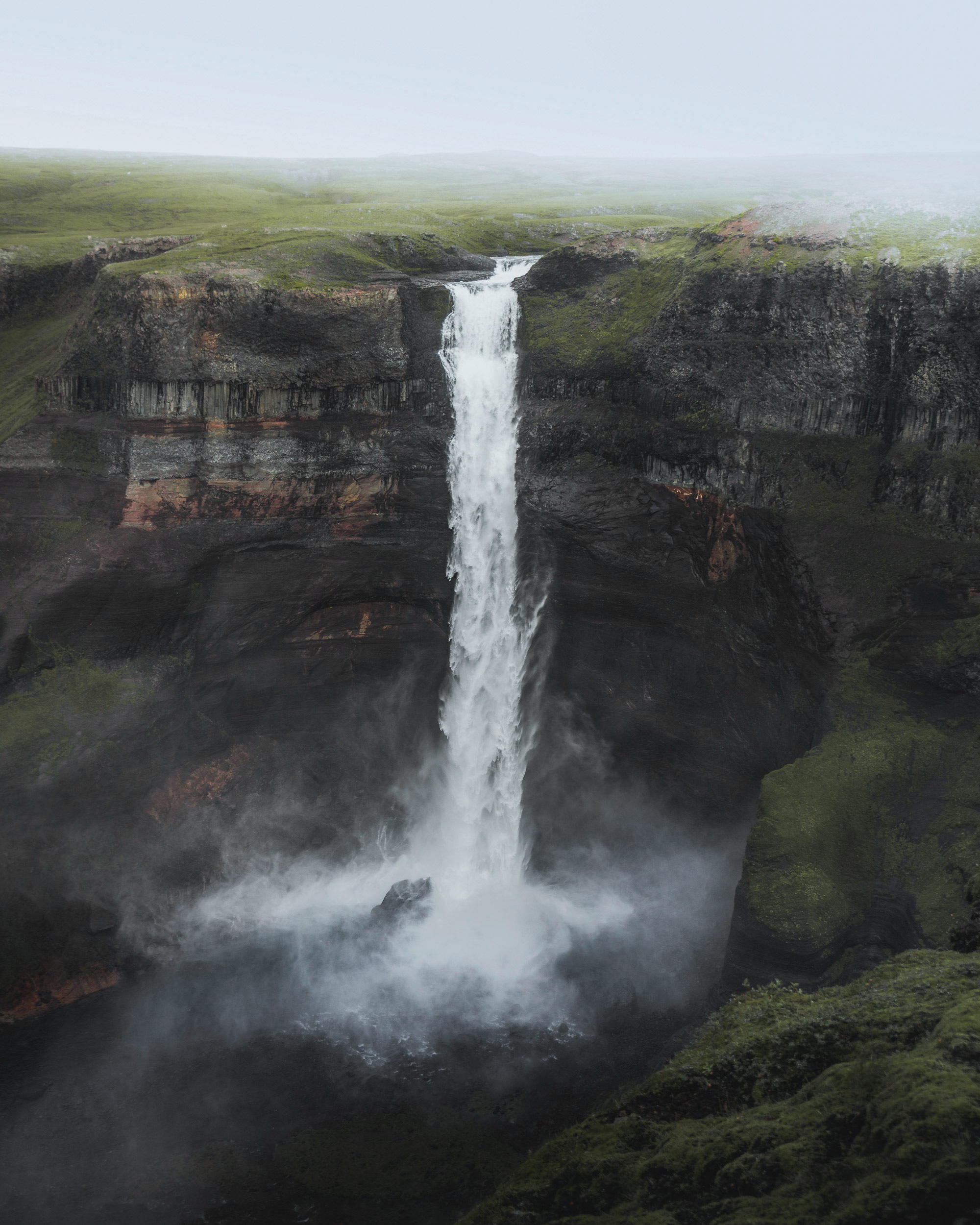 A powerful waterfall cascades down a steep cliff face, surrounded by lush greenery and a serene landscape.