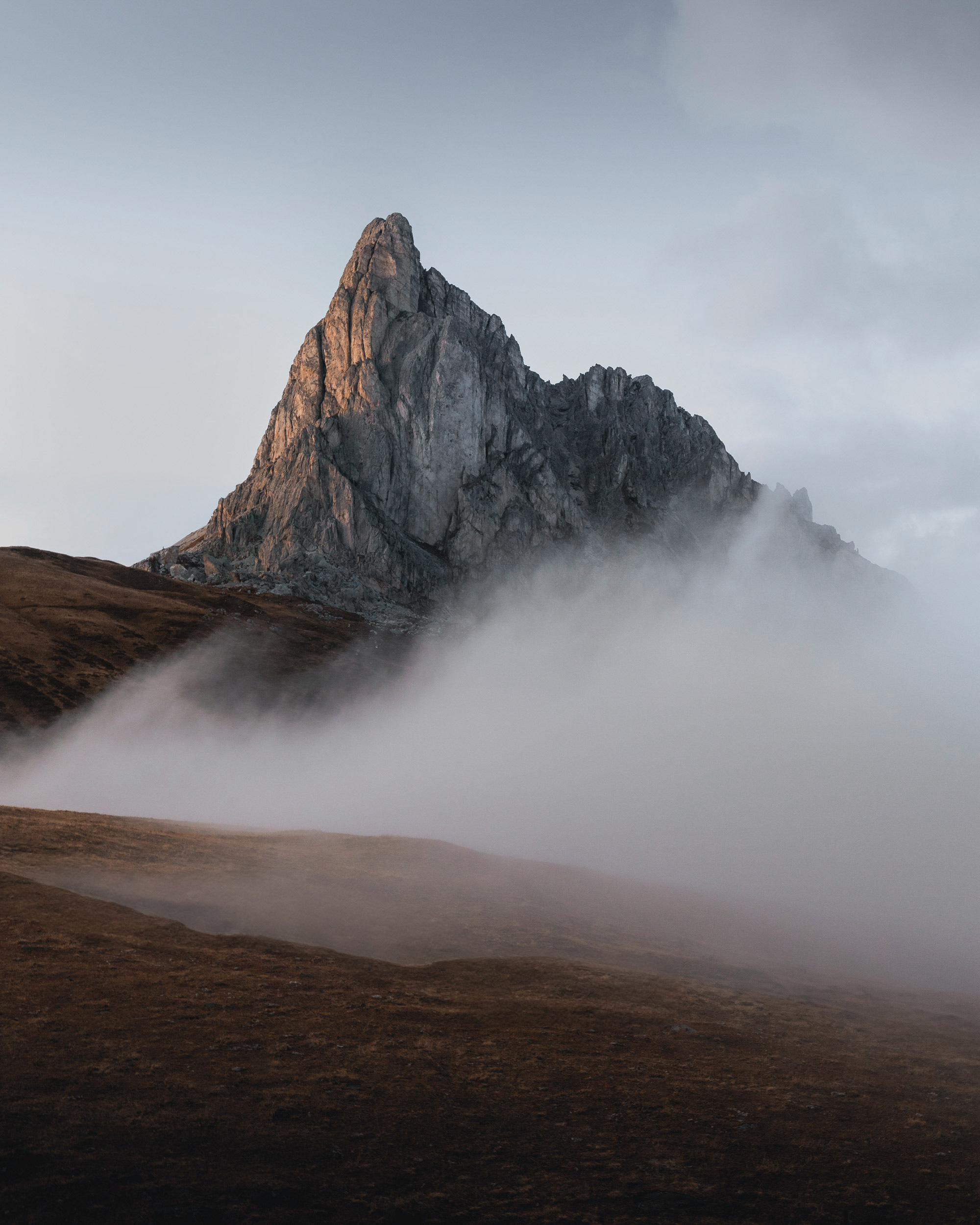 A jagged mountain peak emerging from rolling clouds at dusk.