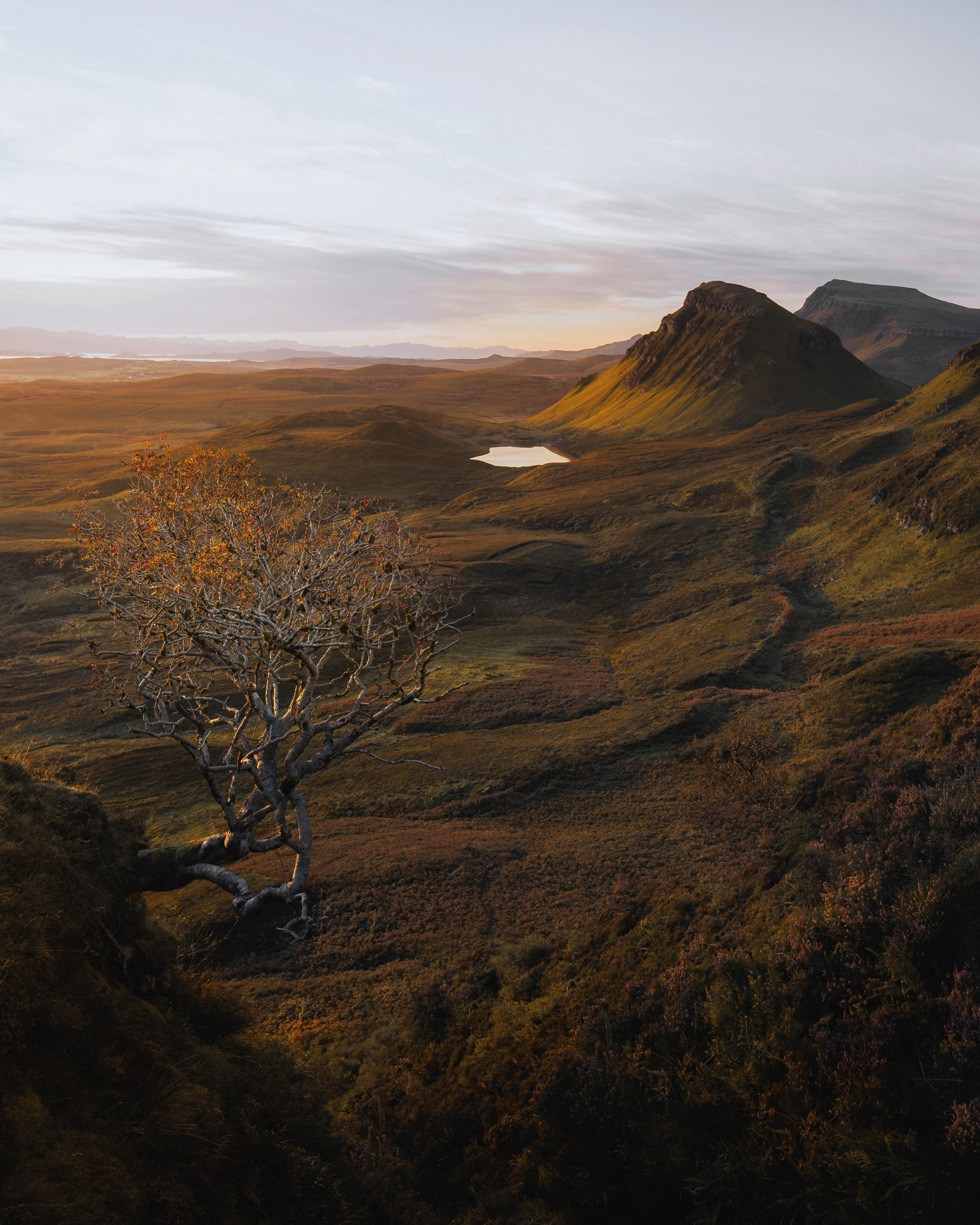 A high-altitude view of the Scottish highlands, showcasing the interplay of light and shadow across the rolling hills and serene lakes.