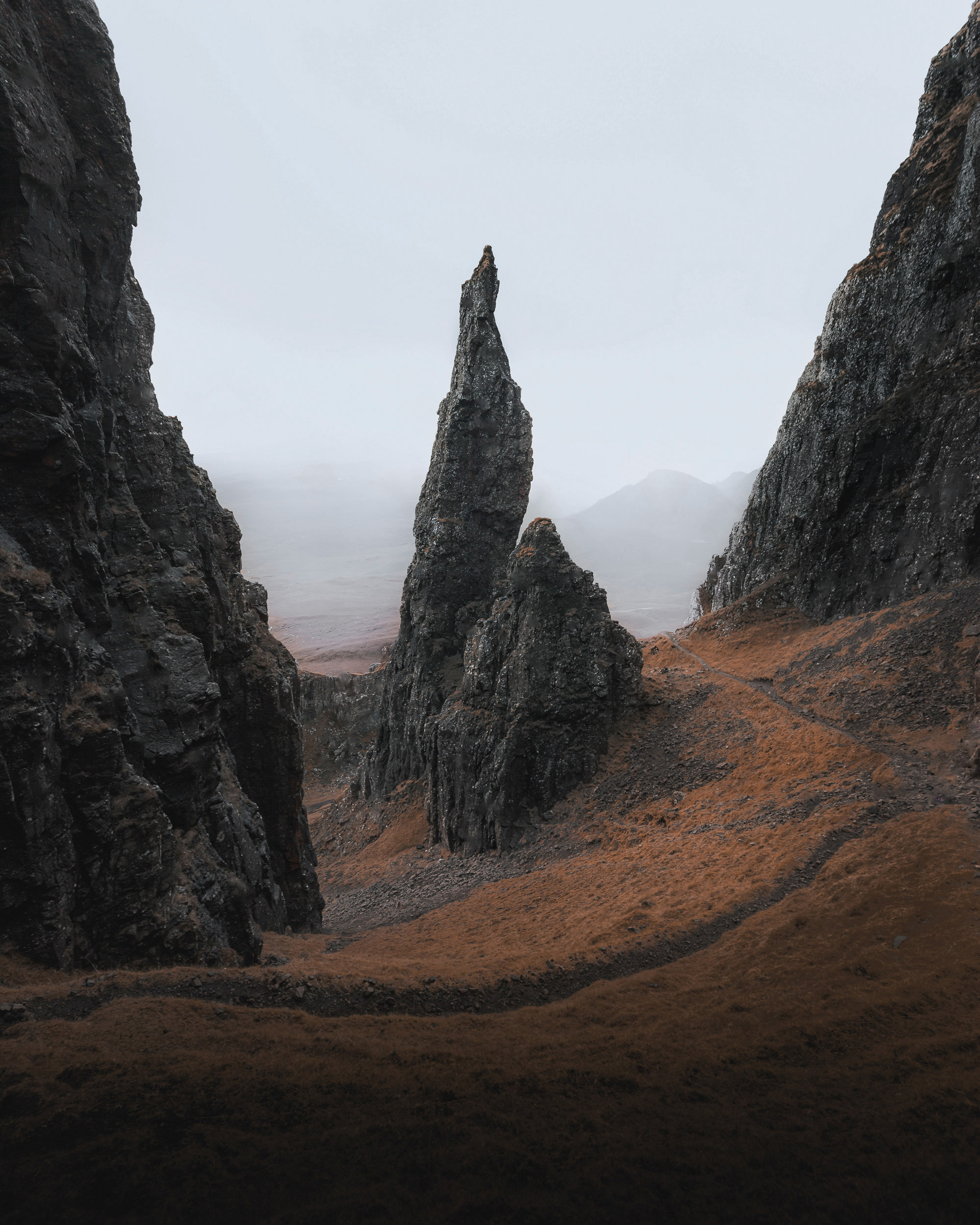 The image features a scenic view of rocky mountains with a path winding through them. The landscape showcases various geological formations, highlighting the effects of erosion on the terrain. The sky above adds depth to the scene, which includes cliffs and outcrops characteristic of badlands and escarpments.