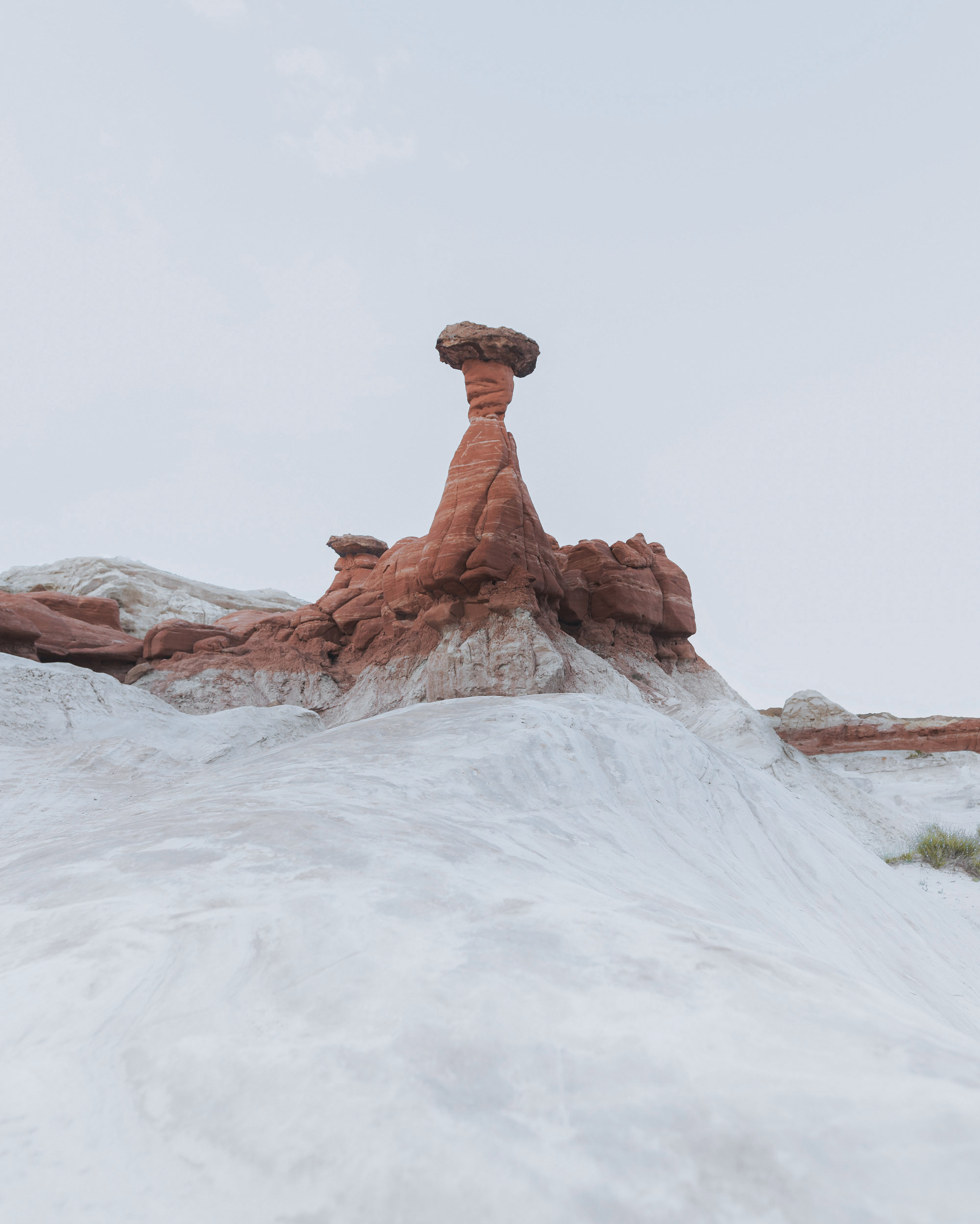 A solitary, reddish-brown hoodoo, sculpted by time and erosion, stands sentinel atop a sloping expanse of pale, almost white, rock formations.