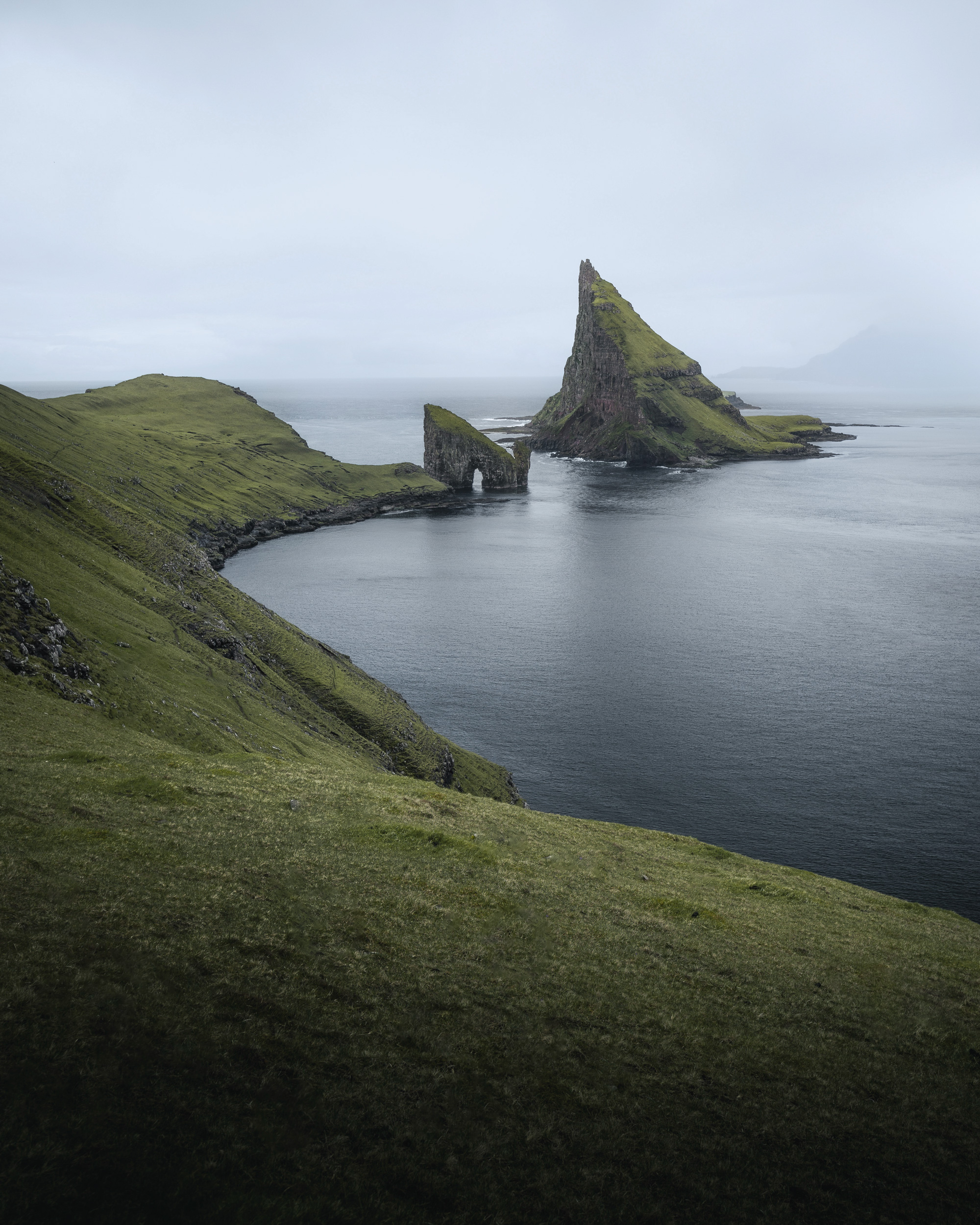 Moody, overcast conditions envelop the geological formations of Drangarnir and Tindhólmur in the remote Faroe Islands.